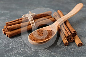 Aromatic cinnamon powder and sticks on grey table, closeup