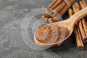 Aromatic cinnamon powder and sticks on grey table, closeup. Space for text