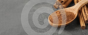 Aromatic cinnamon powder and sticks on grey table, closeup view with space for text. Banner design