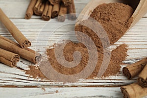 Aromatic cinnamon powder and sticks on white wooden table, closeup