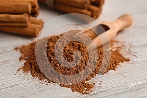 Aromatic cinnamon powder and sticks on white wooden table, closeup