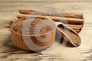 Aromatic cinnamon powder and sticks on wooden table, closeup