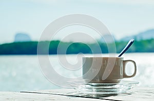 Aromatic coffee white cup in a blurry riverside view landscape background in sunshine