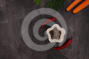 Aromatic colored peppers in a white star shaped bowl surrounded by two hot chili peppers on a dark metallic background with