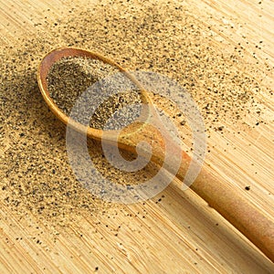 Aromatic fresh powdered black pepper ground, in spoon on wooden bamboo cutting board