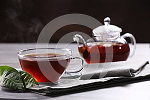 Aromatic hot tea in glass cup, teapot and leaves on light table. Space for text