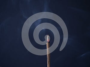 Aromatic incense stick is burning with beautiful gray curls of smoke on a dark blue background in a meditation room.