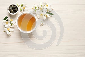 Aromatic jasmine tea, dry leaves and fresh flowers on white wooden table, flat lay. Space for text