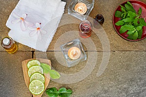 Aromatic oil, burned candle, pink flowers, sliced lime, green leaf, white towel on vintage grunge stone background
