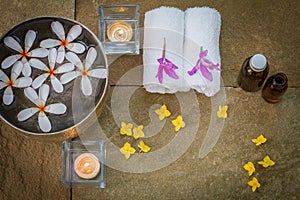 Aromatic oil, burned candle, pink yellow flowers, white towel on vintage grunge stone background