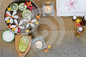 Aromatic oil, burned candle, pink yellow orange flowers, sliced lime, white towel on vintage grunge stone background