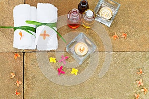 Aromatic oil, burned candle, pink yellow orange flowers, white towel on vintage grunge stone background