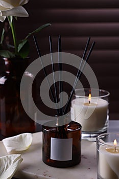 Aromatic reed air freshener and burning candles on white board near window