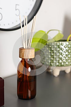 Aromatic reed air freshener near houseplant on gray table indoors