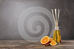 Aromatic reed air freshener, slice of orange and cinnamon stick on wooden table against grey background