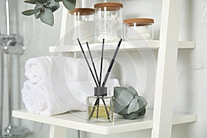 Aromatic reed air freshener, toiletries and rolled towels on white wooden shelf in bathroom