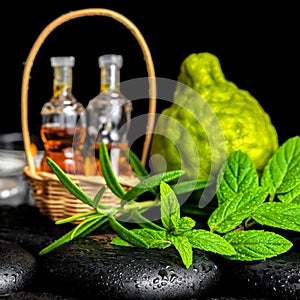 Aromatic spa of bottles essential oil in basket, fresh mint, rosemary and bergamot fruits on black zen basalt stones with