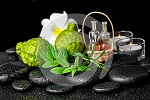 Aromatic spa of bottles essential oil in basket, fresh mint, rosemary, bergamot fruits, flower and candles on black zen stones