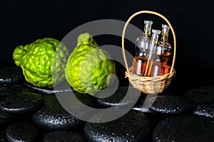 Aromatic spa concept of bottles essential oil in basket, bergamot and zen basalt stones with dew on black background, closeup