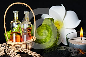 Aromatic spa concept of bottles essential oil in basket, flower, bergamot, candles and black zen basalt stones with dew