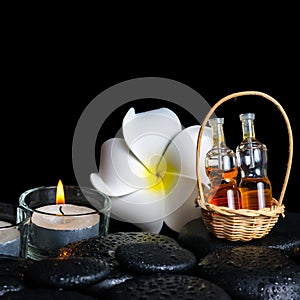 Aromatic spa setting of plumeria flower, candles and bottles essential oil on zen stones, closeup