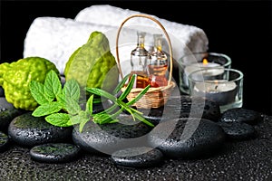 Aromatic spa still life of bottles essential oil, fresh mint, rosemary, bergamot fruits, towels and candles on zen stones