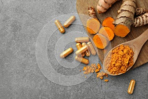 Aromatic turmeric powder, pills and raw roots on grey table, flat lay. Space for text