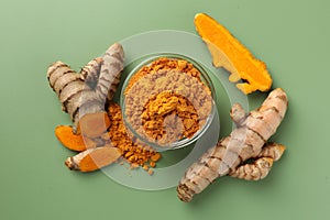 Aromatic turmeric powder and raw roots on green background, flat lay