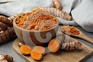 Aromatic turmeric powder and raw roots on grey table, closeup