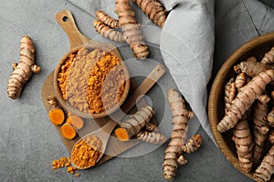 Aromatic turmeric powder and raw roots on grey table, flat lay