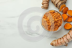 Aromatic turmeric powder and raw roots on white marble table, flat lay. Space for text