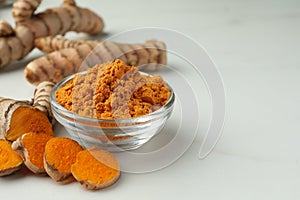 Aromatic turmeric powder and raw roots on white table, closeup. Space for text