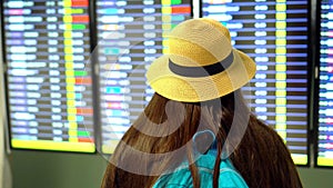 Aroport. The girl with long dark hair with a straw hat checks embarkation of the airplane. Woman looking at timetable