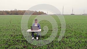 Around drone fly view of young man working remotely with laptop outside alone isolated on spring meadow. Student typing