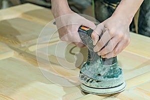 Ð¡arpenter polishes the wooden surface of the door leaf. Electric eccentric orbital grinding machine.