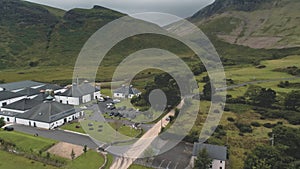 Arran whiskey distillery aerial. Road in green mountains valley. Scottish village with houses, camp