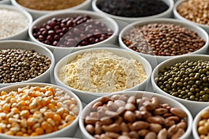 Arranged white bowls with uncooked pulses, grains and seeds on w