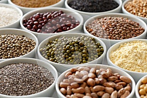 Arranged white bowls with uncooked pulses, grains and seeds on w