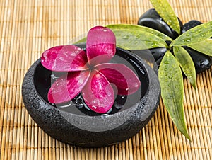 Arrangement of black zen stone with red plumeria flower on wooden bacground