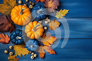 Arrangement of orange and blue mini pumpkins, vibrant yellow leaves on a textured blue wooden surface. Fall background with