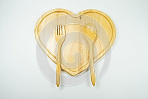 Arrangement of spoons and forks on a heart-shaped wooden plate on a white background.