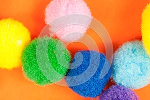 Arrangement of vivid colorful fluffy fuzzy textile soft balls on vibrant orange paper background