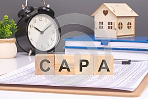 'CAPA' on wooden blocks, with a small house and alarm clock, conveys implementing corrective actions for photo