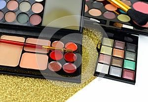 An array of makeup or cosmetics scattered over a gold glitter background. Shallow depth of field puts emphasis on lipsticks.