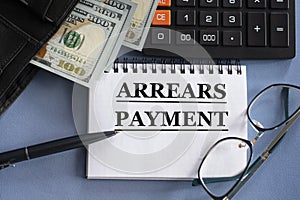 ARREARS PAYMENT - words in a notebook against the background of money, glasses and calculator