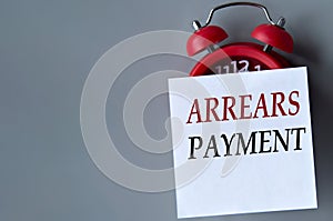 ARREARS PAYMENT - words on a white piece of paper on a gray background. Red alarm clock with white piece of paper