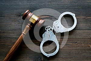 Arrest concept. Metal handcuffs near judge gavel on dark wooden background top view