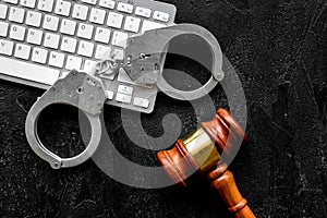 Arrest of a hacker for cyber fraud concept. Handcuff near keyboard and judge gavel on black background top view