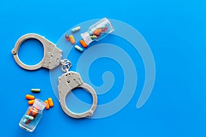 Arrest for illegal purchase, possession and sale drugs concept. Drugs as pills near handcuff on blue background top view