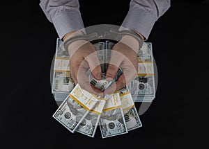 An arrested male official in handcuffs holds stacks of dollars in his hands received as a bribe. A dishonest official is